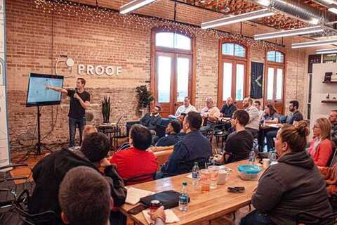 Presenter with a microphone pointing at a screen for a seated loft workshop audience