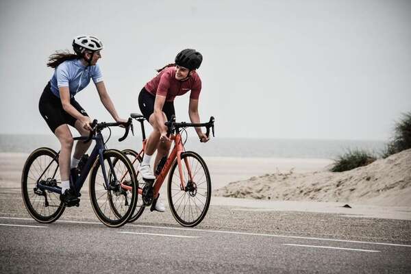Two cyclists in jerseys riding a coastal road beside beach dunes