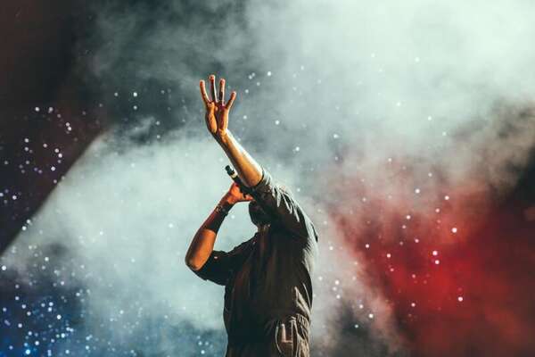 Silhouetted performer raising an arm into teal and red stage haze