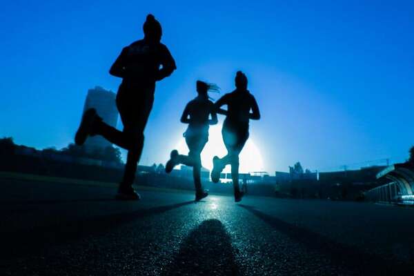 Silhouetted runners on a track at sunrise with a tower on the horizon