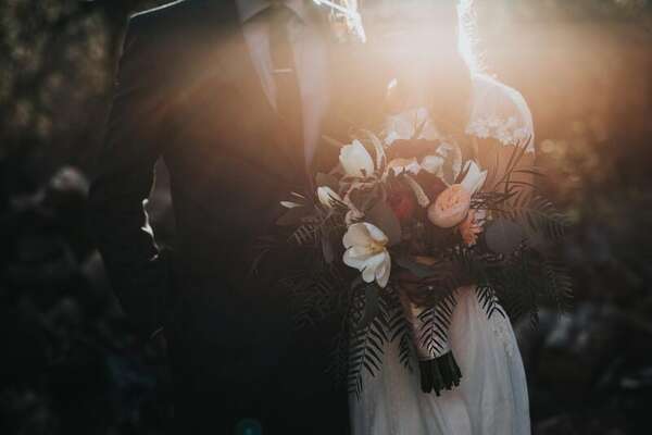 Bride and groom with a bouquet lit by a golden-hour sun flare